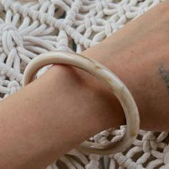 Person wearing a beige bracelet on a textured white surface