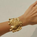 Hand wearing a gold bracelet against a neutral background