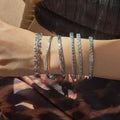 Close-up of a person's wrist wearing multiple silver bracelets on a patterned fabric background