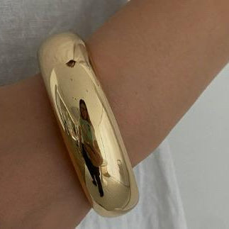 Gold bracelet on a wrist against a neutral background