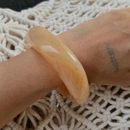 Hand wearing a peach-colored bracelet on a textured white surface