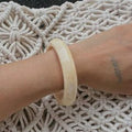 Close-up of a wrist wearing a beige bracelet on a textured white surface