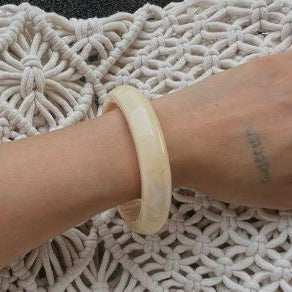Close-up of a wrist wearing a beige bracelet on a textured white surface