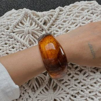 Hand wearing a large amber bracelet on a textured white surface