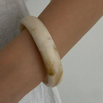 Beige bracelet on a wrist against a neutral background