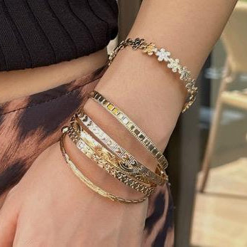 Close-up of a wrist wearing multiple gold bracelets with a blurred background