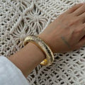 Gold bracelet on a wrist against a textured white background