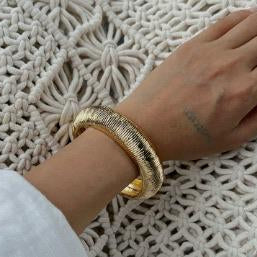 Gold bracelet on a wrist against a textured white background