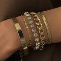 Gold bracelets with chain and crystal designs on a wrist against a dark background