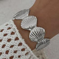 Silver shell bracelet on a wrist with a white lace garment background