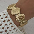 Gold shell bracelet on a wrist with a textured white sleeve.
