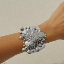 Hand wearing a silver bracelet with a large, intricate clasp on a neutral background