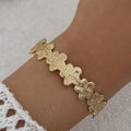 Gold floral bracelet on a wrist with a neutral background