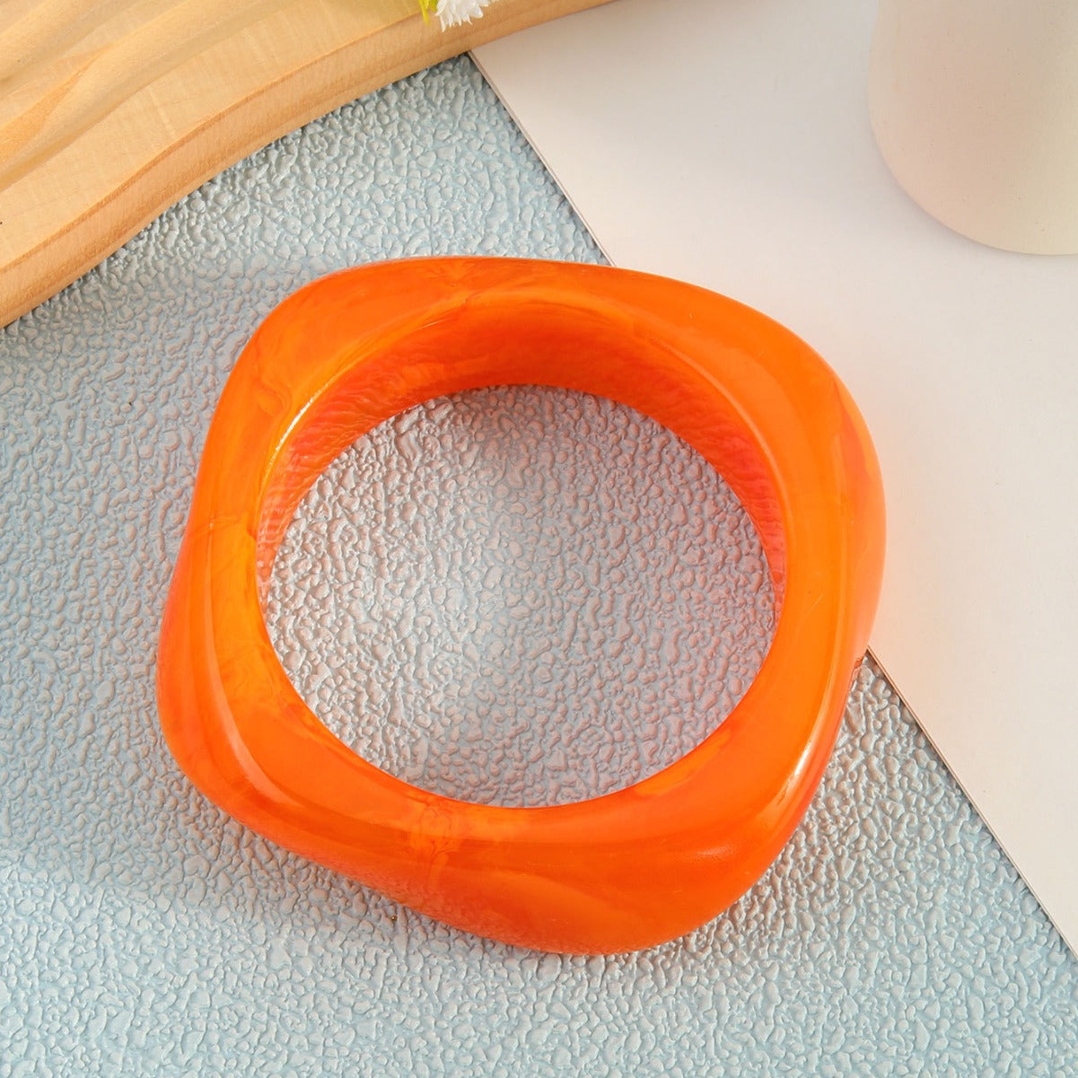 Orange plastic ring on a textured surface with a wooden block and white flowers in the background