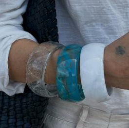 Close-up of a person's wrist wearing a blue bracelet with a white shirt sleeve.