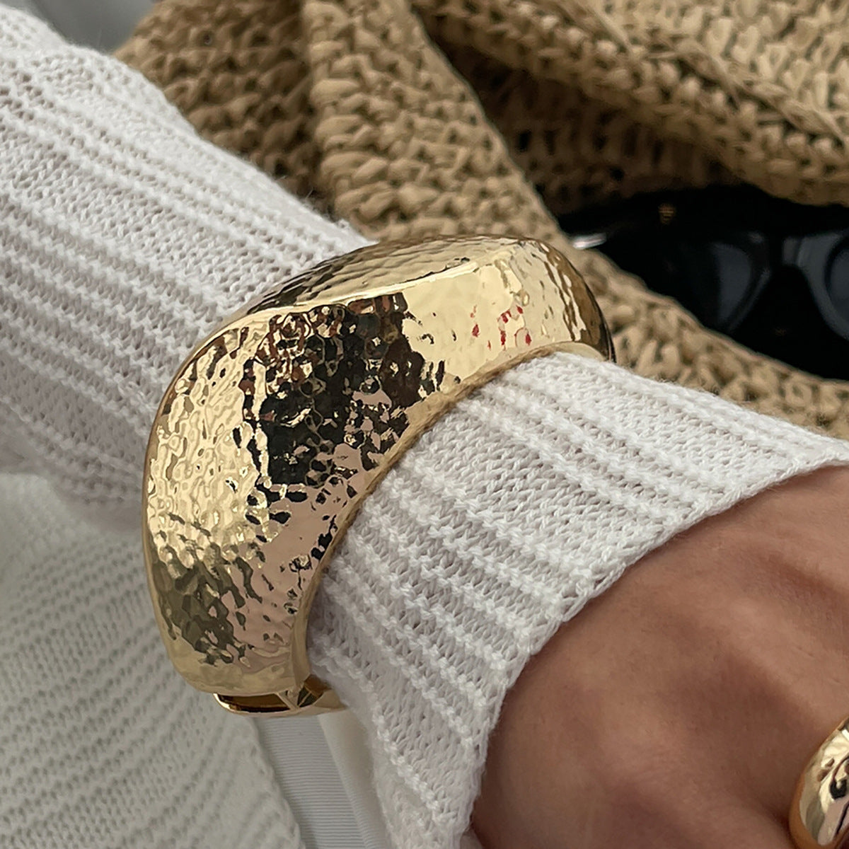 Gold bracelet on a wrist with a textured surface, worn over a white sleeve.
