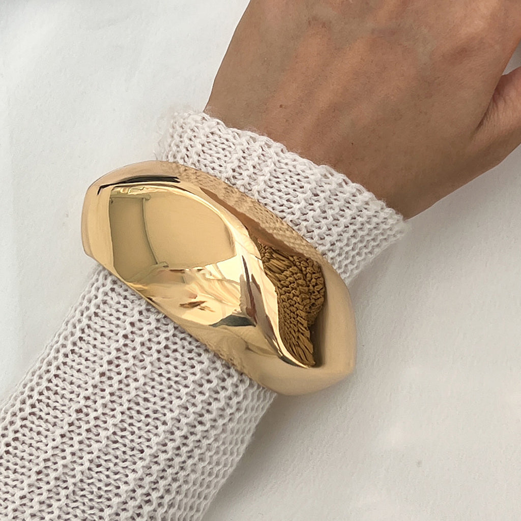 Gold ring on a hand wearing a white textured sleeve against a light background
