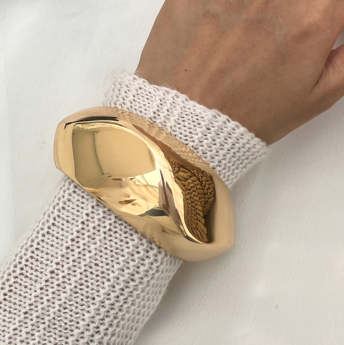 Gold ring on a hand wearing a white textured sleeve against a light background