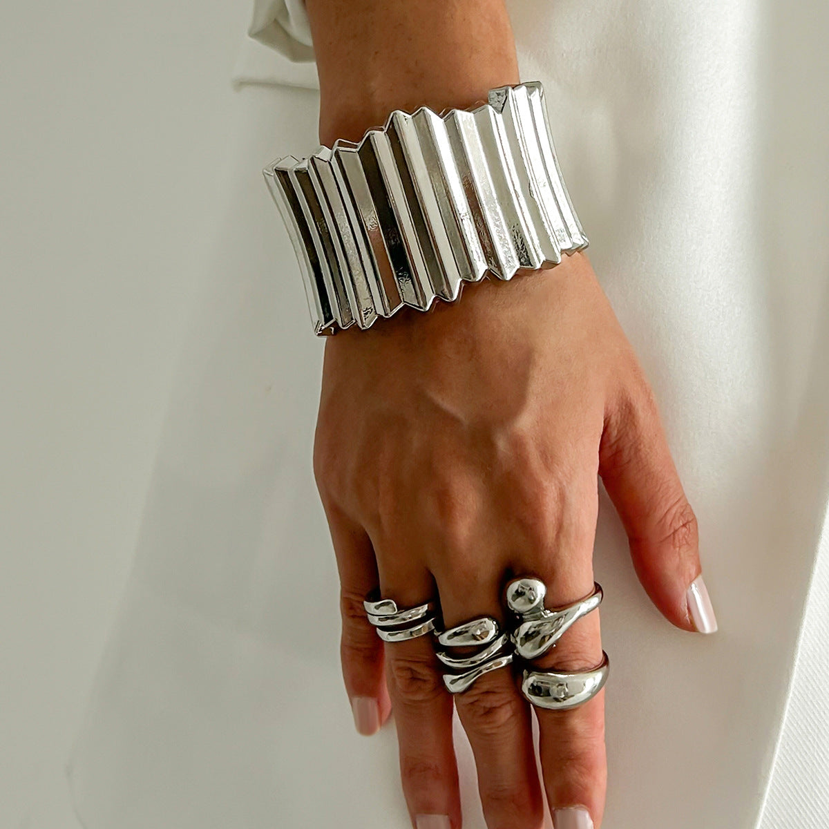 Hand wearing a silver bracelet and multiple rings on a plain background