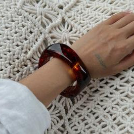 Hand wearing a tortoiseshell bracelet on a textured surface