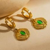 Gold earrings with green gemstones on a beige background
