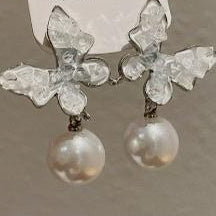 Silver earrings with clear gemstones and pearls held by a hand against a neutral background