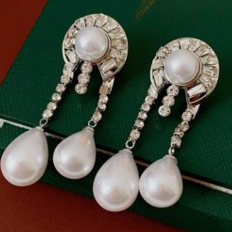 Pair of pearl earrings with rhinestone accents on a green box background