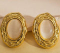 Pair of gold earrings with a beige stone on a beige background