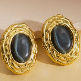 Pair of gold-framed earrings with dark stones on a beige background