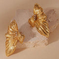 Gold butterfly-shaped earrings on a textured stone surface with a beige background