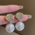 Pearl earrings with gold accents held between fingers against a neutral background