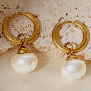 Gold hoop earrings with pearl drops on a textured stone surface