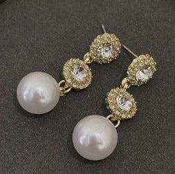 Gold earrings with pearl drops on a gray surface