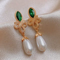 Gold earrings with green gemstones and pearl drops on a beige fabric background