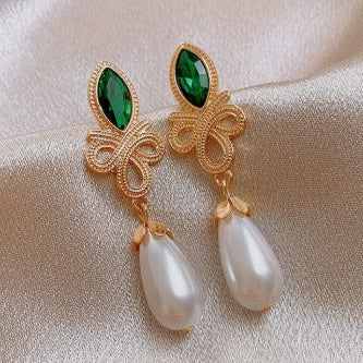Gold earrings with green gemstones and pearl drops on a beige fabric background