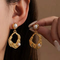 Gold earrings with pearl accents worn by a person against a neutral background
