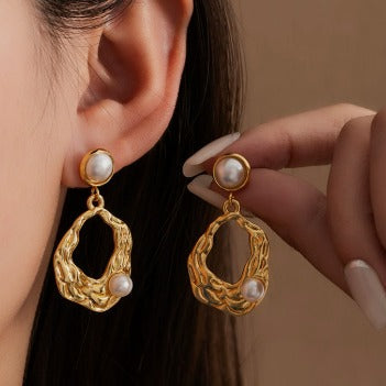 Gold earrings with pearl accents worn by a person against a neutral background