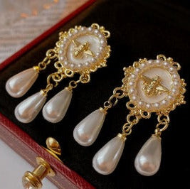 Gold and pearl earrings on a dark surface with a red box.