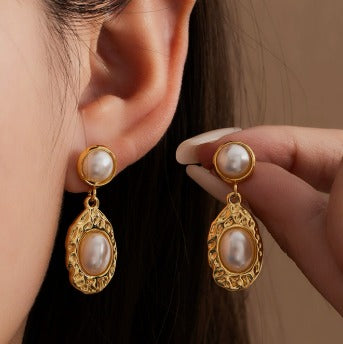 Gold earrings with pearl drops worn by a person against a neutral background