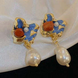 Pair of gold earrings with pearls and red stones on a white fabric background