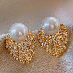 Pair of gold earrings with pearl-like stones on a beige fabric background