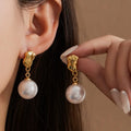 Gold earrings with pearl drops worn by a person against a neutral background
