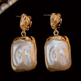 Gold-framed earrings with a pearl-like center on a dark background