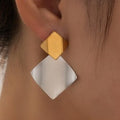 Gold and silver geometric earrings worn by a person.