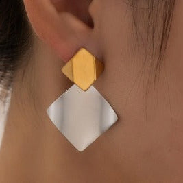 Gold and silver geometric earrings worn by a person.