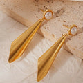 Gold earrings with pearl accents on a textured beige surface