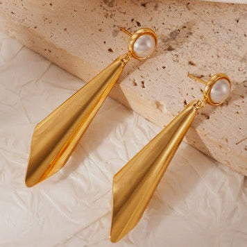 Gold earrings with pearl accents on a textured beige surface