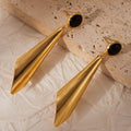 Gold earrings with black stones on a textured beige surface