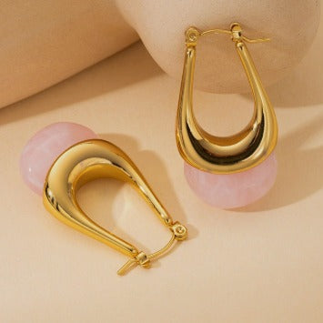 Gold hoop earrings with pink spherical charms on a beige background