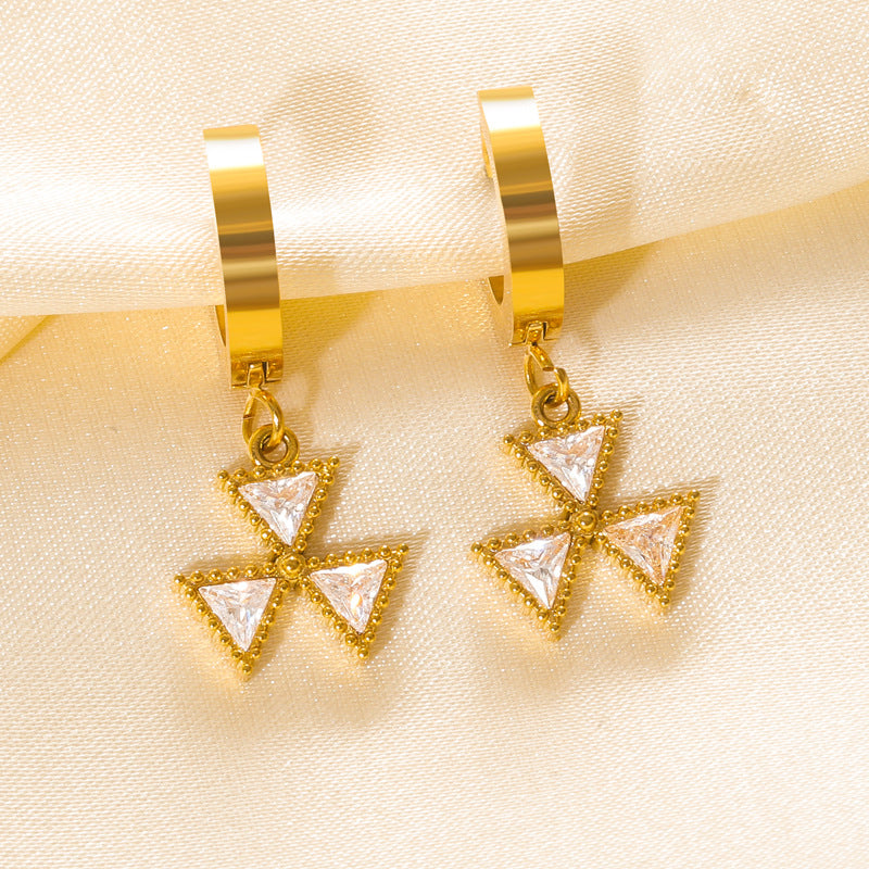 Gold earrings with triangle-shaped charms on a beige fabric background